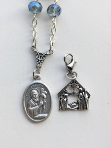This is a close up of the mSt Andrew medal and Nativity charm novena tracker on the blue St Andrew Chaplet on a white background. 