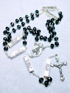 A deep blue mysteries rosary lays on a white background. 