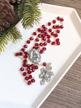 Load image into Gallery viewer, A red glass rosary with a madonna and child centerpiece lays in a white tray with a pine branch next to it. 
