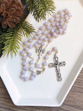 Load image into Gallery viewer, A lilac colored rosary sets in a white tray with a pine branch next to it