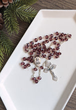 Load image into Gallery viewer, A pirple glass bead rosary lays on a white tray with a pine branch next to it on a wooden background