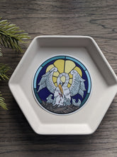 Load image into Gallery viewer, A pelican in her piety round circle sticker sits on a white tray. The background is wood and a decorative plant 
