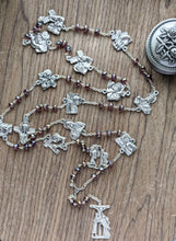 Load image into Gallery viewer, A large stations of the cross chaplet lays in a wooden background with a tosary holder next to it. It features purple crystal glass beads and all 14 stations of the cross depicted on chaplet medals. 