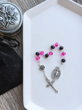 Load image into Gallery viewer, A 10 bead chaple with black and hot pink crystal.glass beads for the hail mary beads and a medal rose bead for the Our Father Bead lays on a white tray. A moraculous medal is attache to one end and a small decorative crucifx is attached to the other aide. The tray lays on a wood background with a rosary holder next to it. 