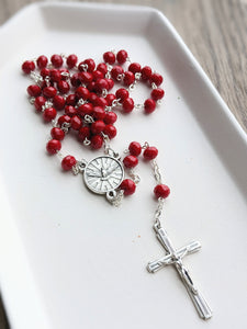 A solid red bead rosary lays in a white tray. 