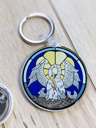 A Pelican in her Piety symbol is on a circular keychain laying on a wooden background. 