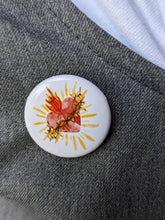 Load image into Gallery viewer, A watercolor style sacred heart is on a white background button pin attached to a grey and white cloth for background. 