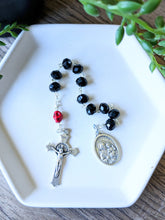 Load image into Gallery viewer, A black glass bead pocket rosary with a red colored skull for the our father bead sits in a white tray with a wooden background