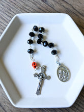 Load image into Gallery viewer, A black glass bead pocket rosary with an orange colored skull for the our father bead sits in a white tray with a wooden background