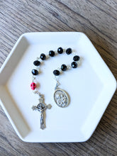 Load image into Gallery viewer, A black glass bead pocket rosary with a hot pink colored skull for the our father bead sits in a white tray with a wooden background