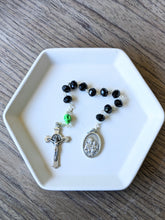 Load image into Gallery viewer, A black glass bead pocket rosary with a lime green colored skull for the our father bead sits in a white tray with a wooden background