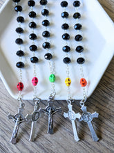 Load image into Gallery viewer, 5 black glass bead pocket rosaries featuring a different colored skull all set in a white tray with a wooden background