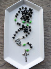 Load image into Gallery viewer, A black rosary with lime green skulls lays on a white tray. Features a St Joseph Centerpiece and St Benedict Crucifix. 