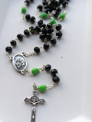A black rosary with lime green skulls lays on a white tray. Features a St Joseph Centerpiece and St Benedict Crucifix. 