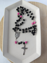 Load image into Gallery viewer, A black rosary with hot pink skulls lays on a white tray. Features a St Joseph Centerpiece and St Benedict Crucifix. 