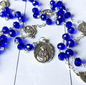 A royal blue seven sorrows chaplets lays on a whitewashed wooden background. 