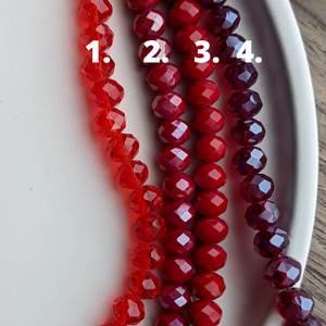 4 shades of red glass beads marked 1-4 are featured on a white dish on a wooden background
