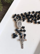 Load image into Gallery viewer, a close up view of the Black St benedict rosary centerpiece and crucifix on a white tray with a wood and fir tree background