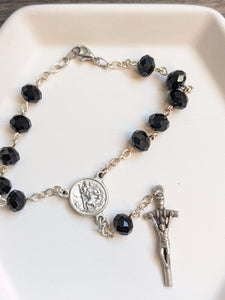 A close up of the black glass bead car rosary with st Christopher centerpiece and JPII style crucifix on a white background