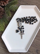 Load image into Gallery viewer, a black glass bead rosary sits on a white tray with a pine branch and wooden background